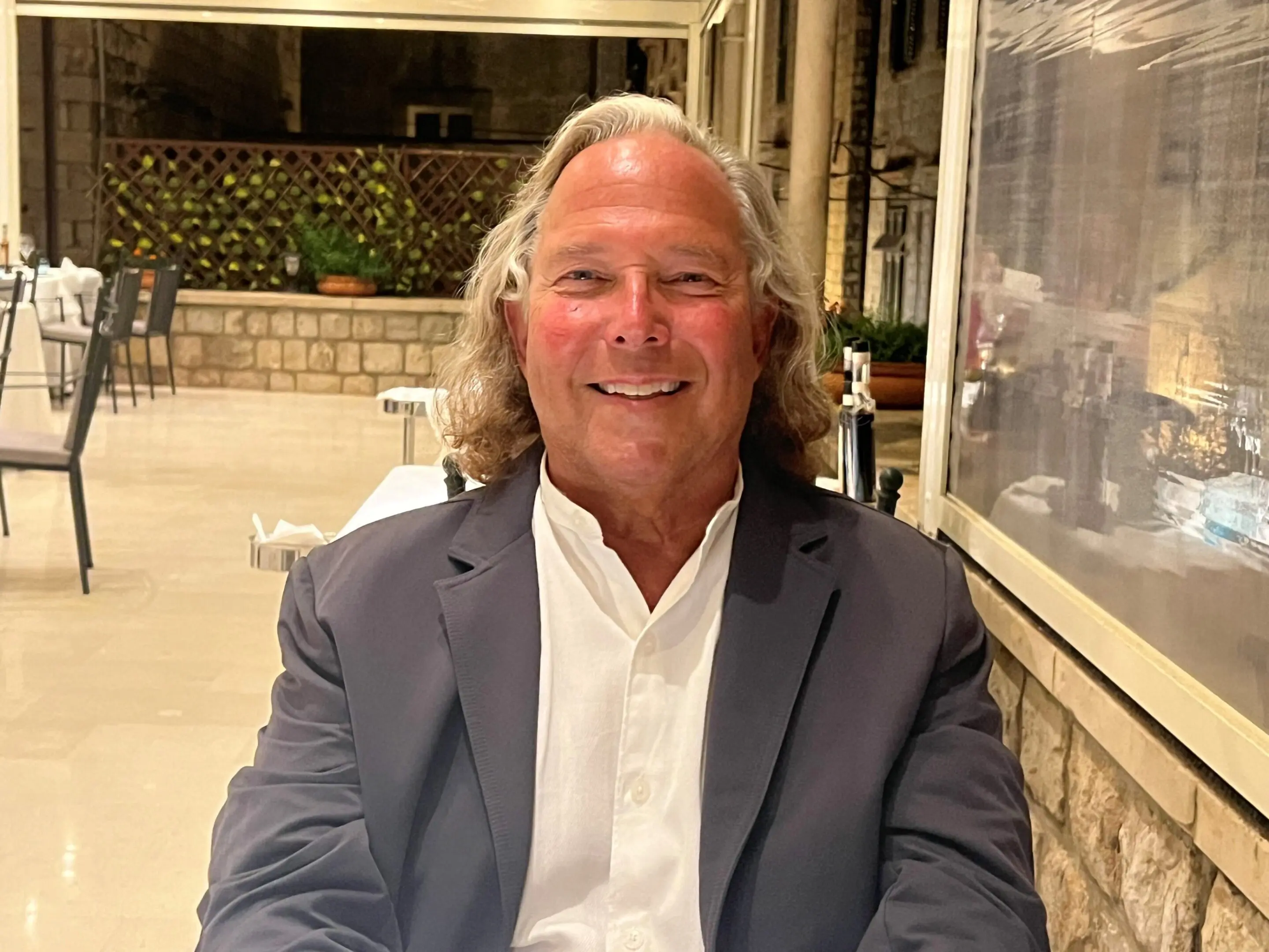Smiling man in a blazer sitting at a restaurant table.